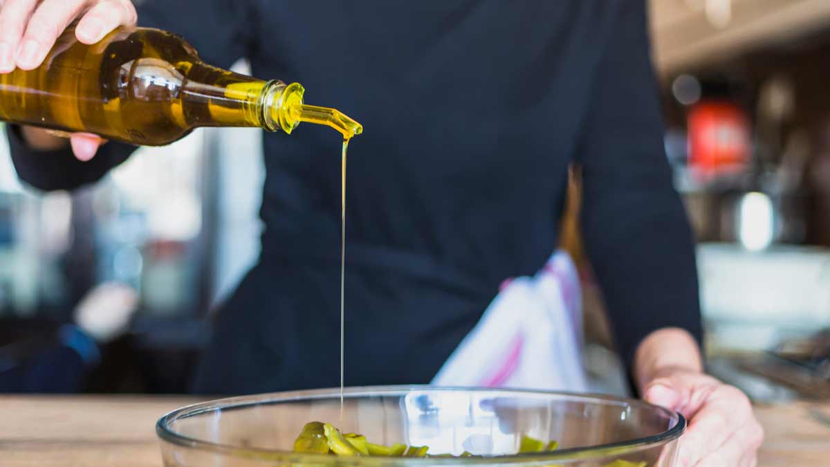 Unas manos de hombre aliñando una ensalada con aceite de oliva virgen extra.